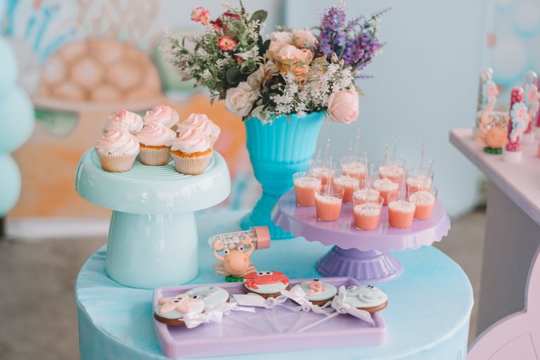 A vibrant dessert table with cupcakes, cookies, flower arrangements, and pastel decorations.